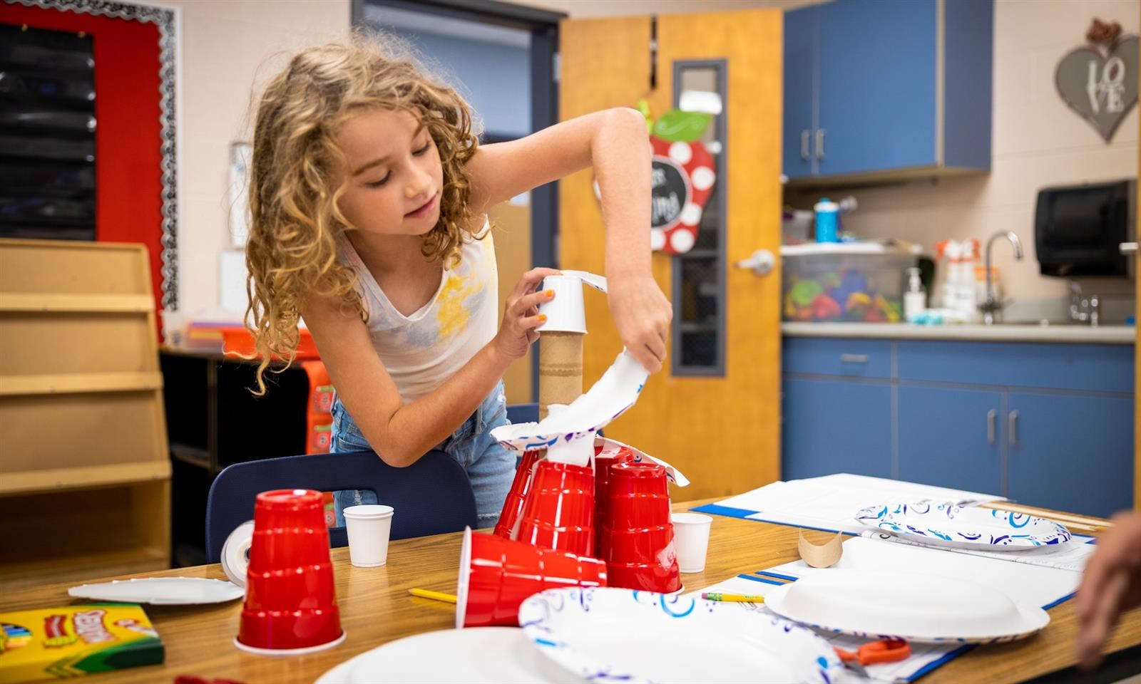 A girl builds a tower out of cups, toilet paper rolls and more